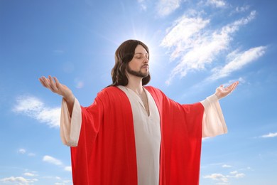 Image of Jesus Christ with outstretched arms against blue sky 