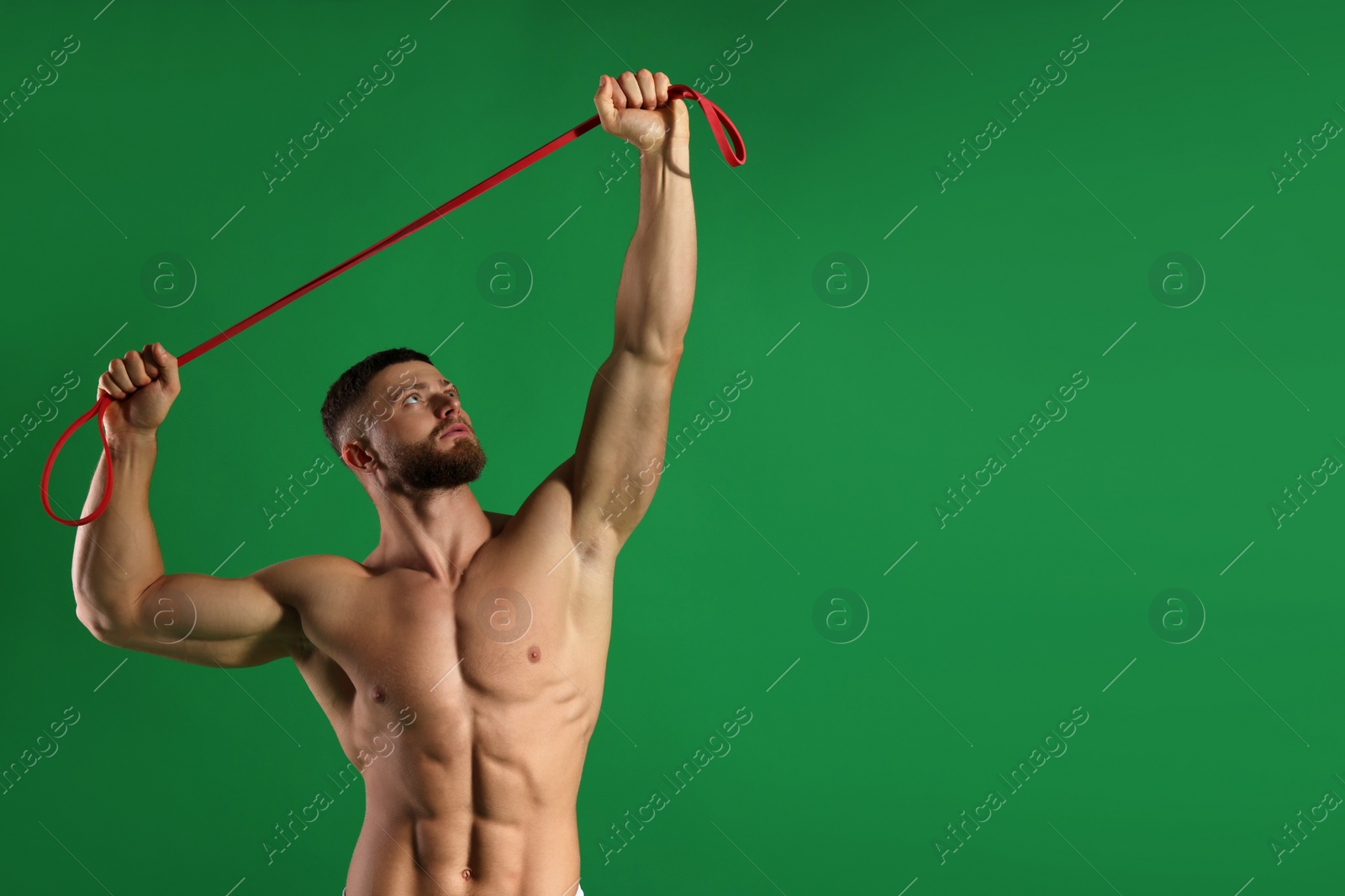 Photo of Muscular man exercising with elastic resistance band on green background. Space for text