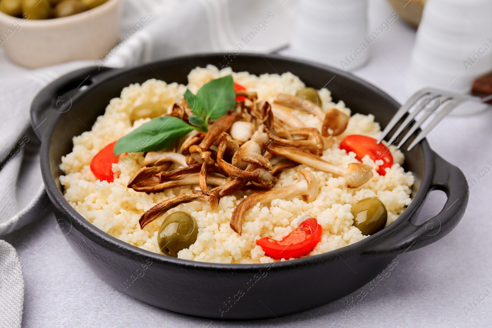 Photo of Tasty couscous with mushrooms, olives and tomatoes served on grey table, closeup