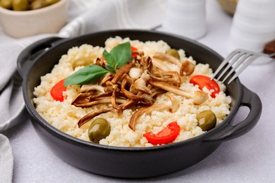 Tasty couscous with mushrooms, olives and tomatoes served on grey table, closeup