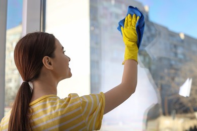 Photo of Young woman cleaning window glass with rag at home