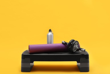 Photo of Step platform, mat, bottle of water and abdominal wheel on yellow background. Sports equipment