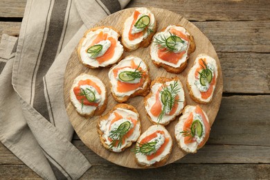 Photo of Tasty canapes with salmon, cucumber, cream cheese and dill on wooden stand, top view