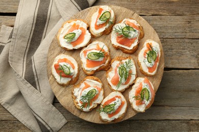 Tasty canapes with salmon, cucumber, cream cheese and dill on wooden stand, top view