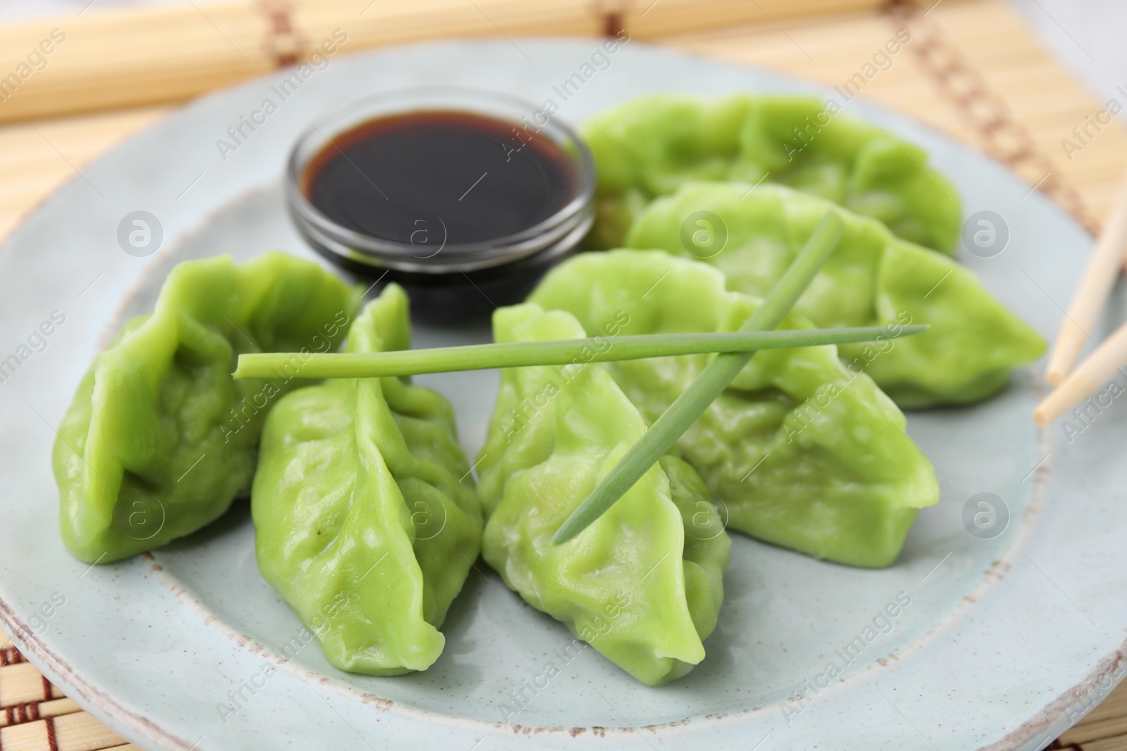 Photo of Delicious green dumplings (gyozas) and soy sauce on plate, closeup