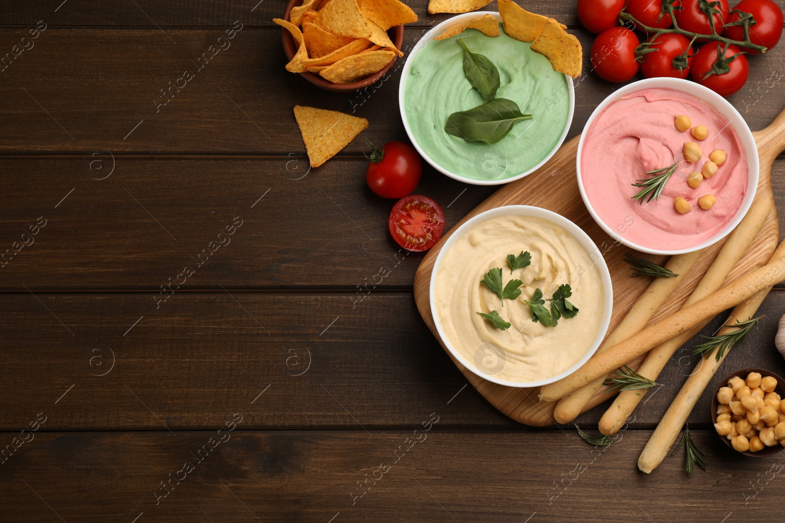 Photo of Different kinds of tasty hummus served with snacks on wooden table, flat lay. Space for text