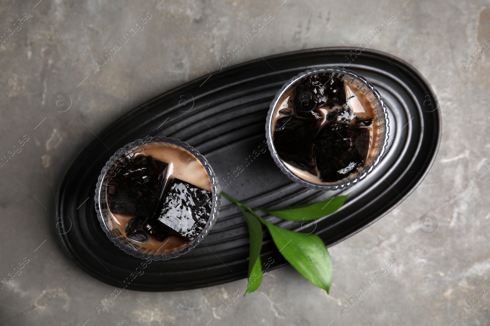 Photo of Glasses of milk with grass jelly and green leaves on grey table, top view