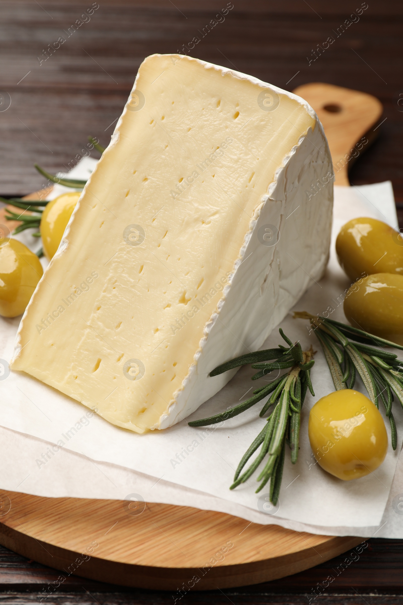 Photo of Board with piece of tasty camembert cheese, olives and rosemary on wooden table, closeup