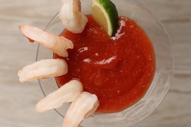 Photo of Tasty shrimp cocktail with sauce and lime in glass on table, top view