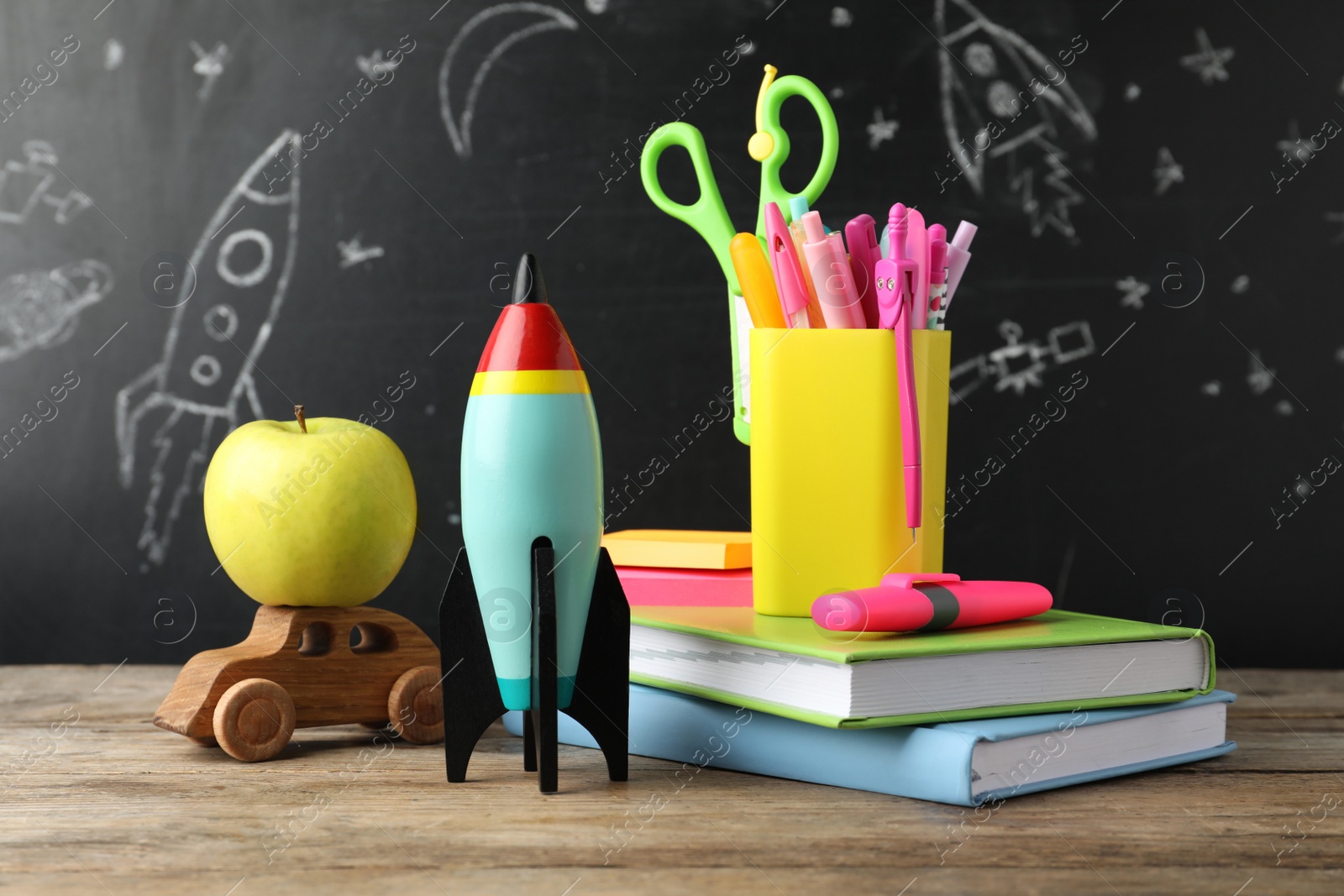 Photo of Bright toy rocket, car and school supplies on wooden table