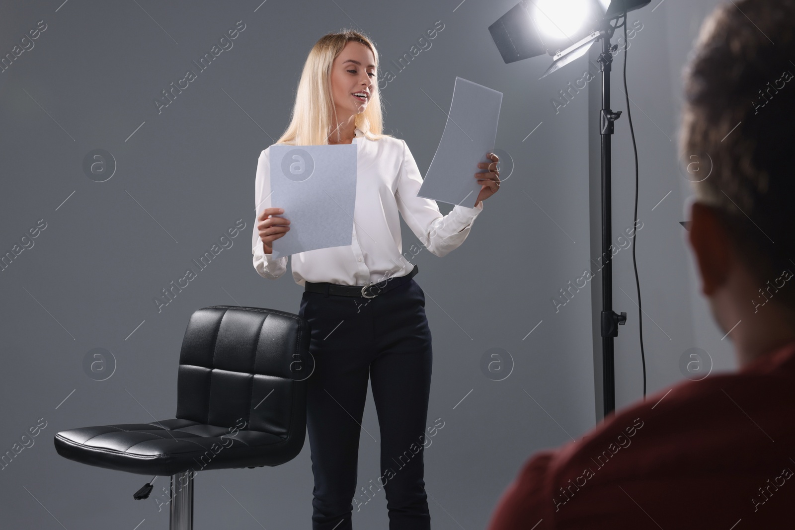 Photo of Emotional woman with script performing in front of casting director against grey background in studio