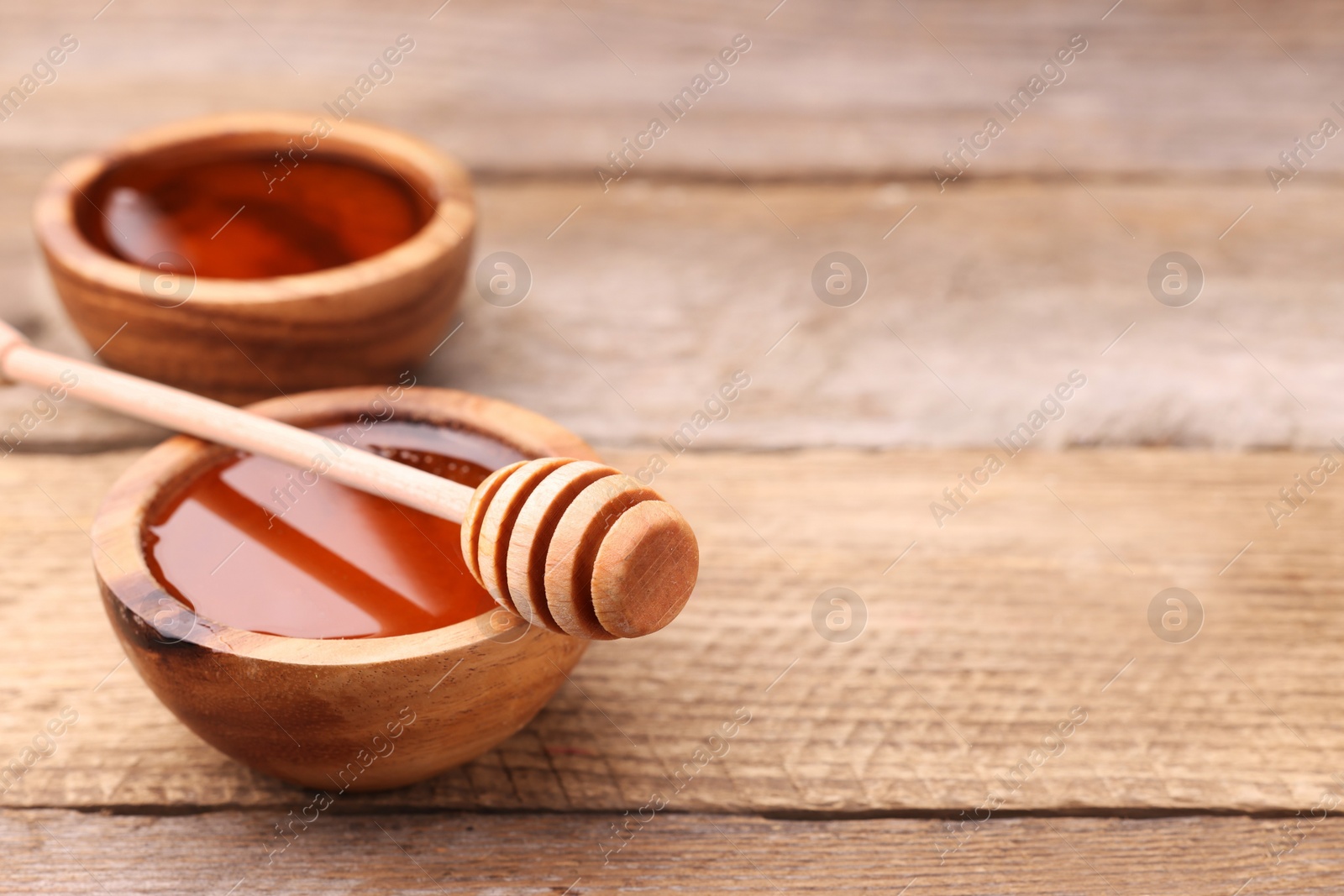 Photo of Delicious honey in bowls and dipper on wooden table. Space for text