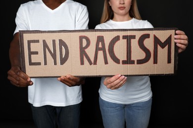 Photo of Young woman and African American man holding sign with phrase End Racism on black background, closeup