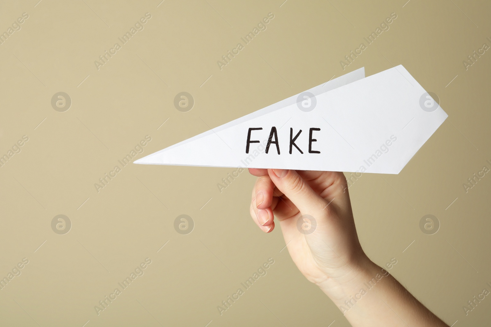 Photo of Woman holding paper plane with word FAKE near beige wall, closeup