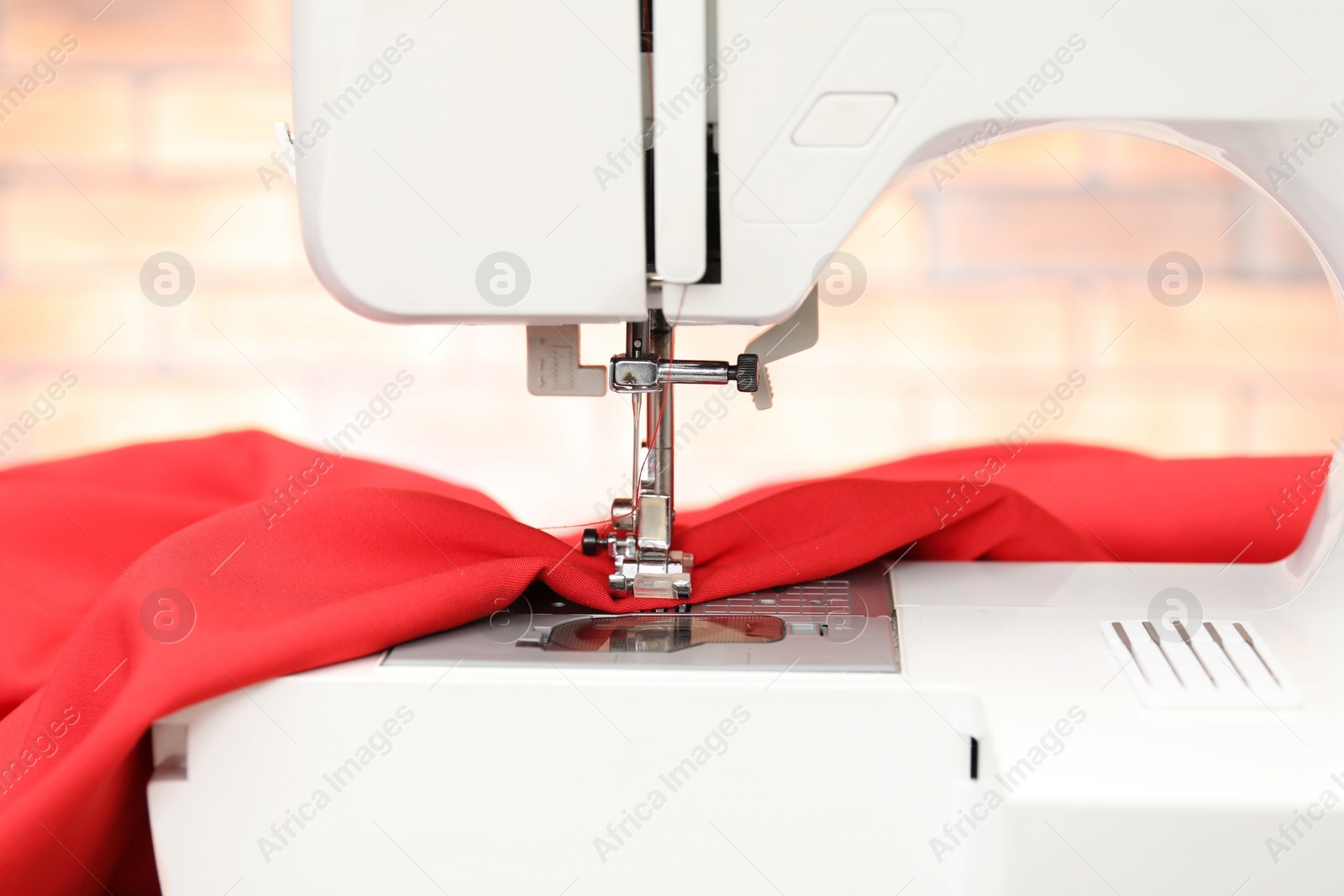 Photo of Sewing machine with red fabric indoors, closeup