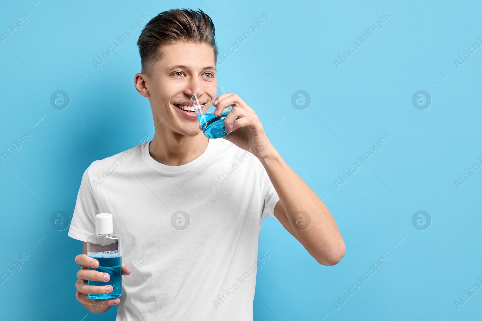 Photo of Young man using mouthwash on light blue background, space for text