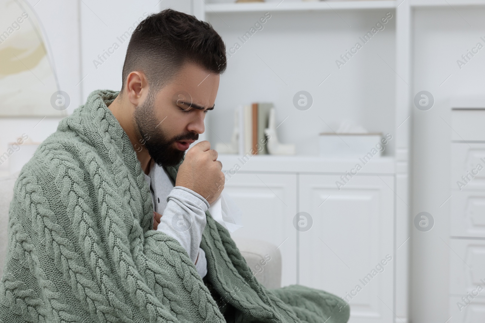Photo of Sick man with tissue coughing at home, space for text