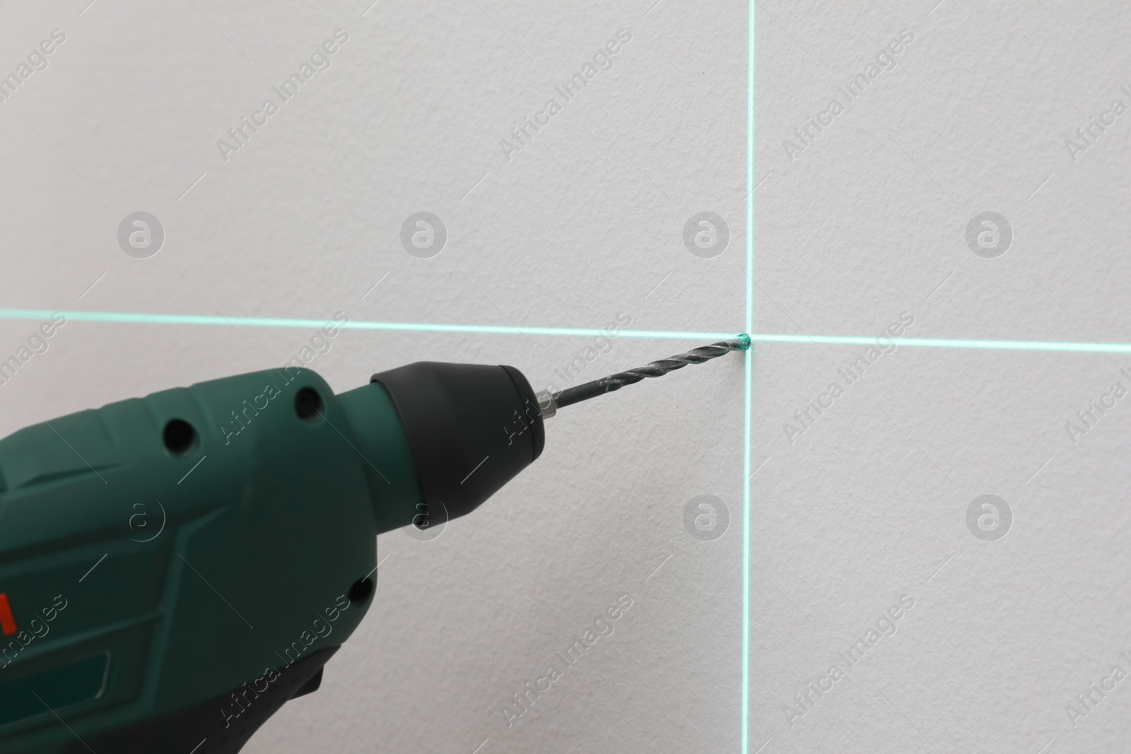 Photo of Using cross line laser level for accurate measurement and drilling hole in grey wall, closeup