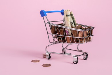 Photo of Small metal shopping cart with money on pink background, space for text