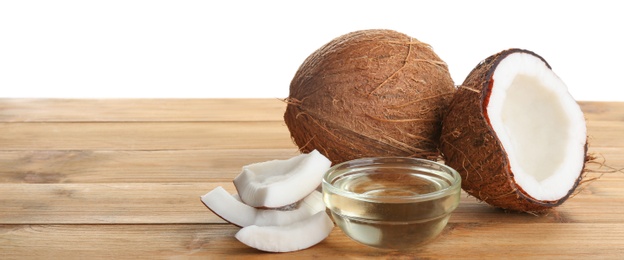 Photo of Ripe coconuts and bowl with natural organic oil on wooden table against white background