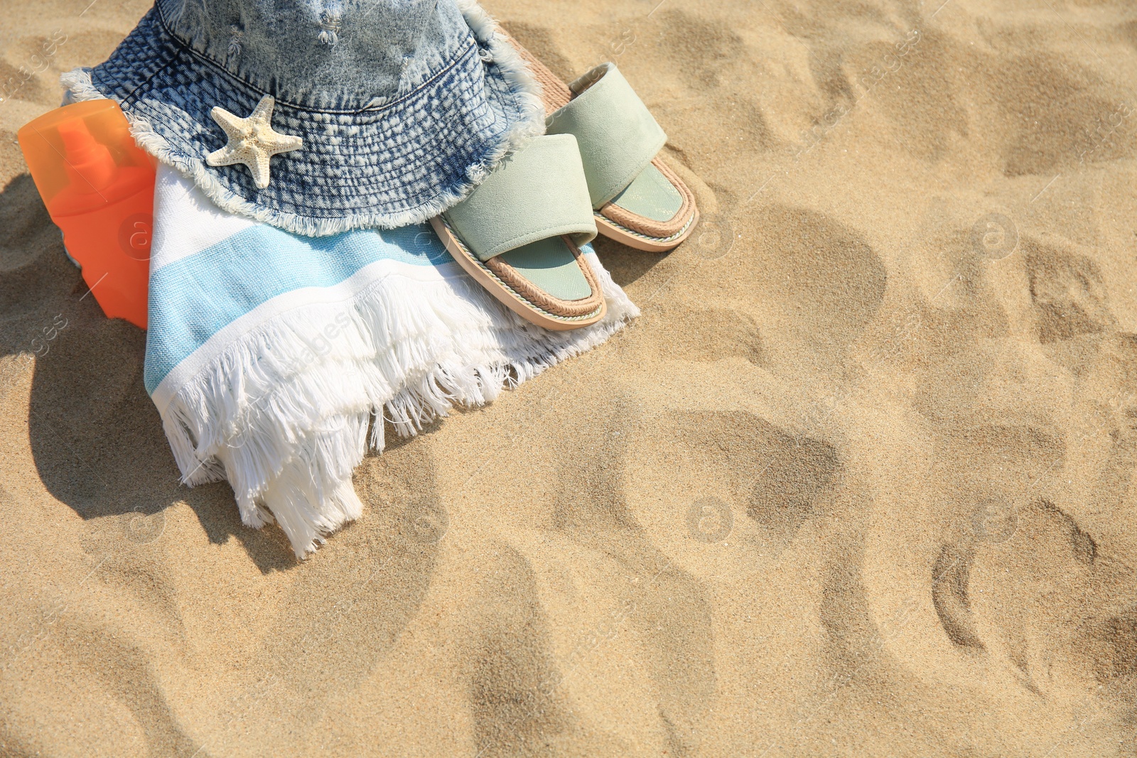 Photo of Denim hat, slippers, towel, starfish and sunscreen on sand, above view. Space for text