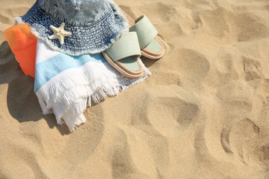 Photo of Denim hat, slippers, towel, starfish and sunscreen on sand, above view. Space for text