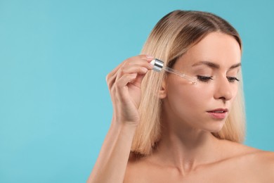 Photo of Beautiful woman applying cosmetic serum onto her face on light blue background, space for text