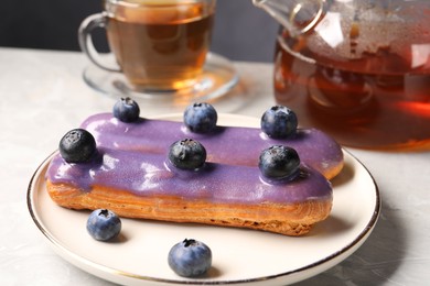 Photo of Tasty glazed eclair with blueberries on grey marble table, closeup