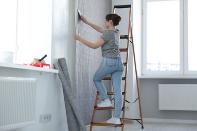 Woman smoothing stylish gray wallpaper in room