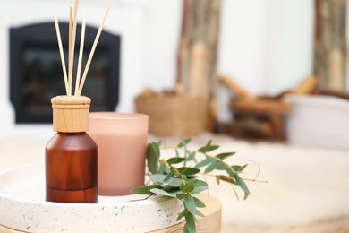 Photo of Reed air freshener with candle and eucalyptus branches on tray indoors, closeup