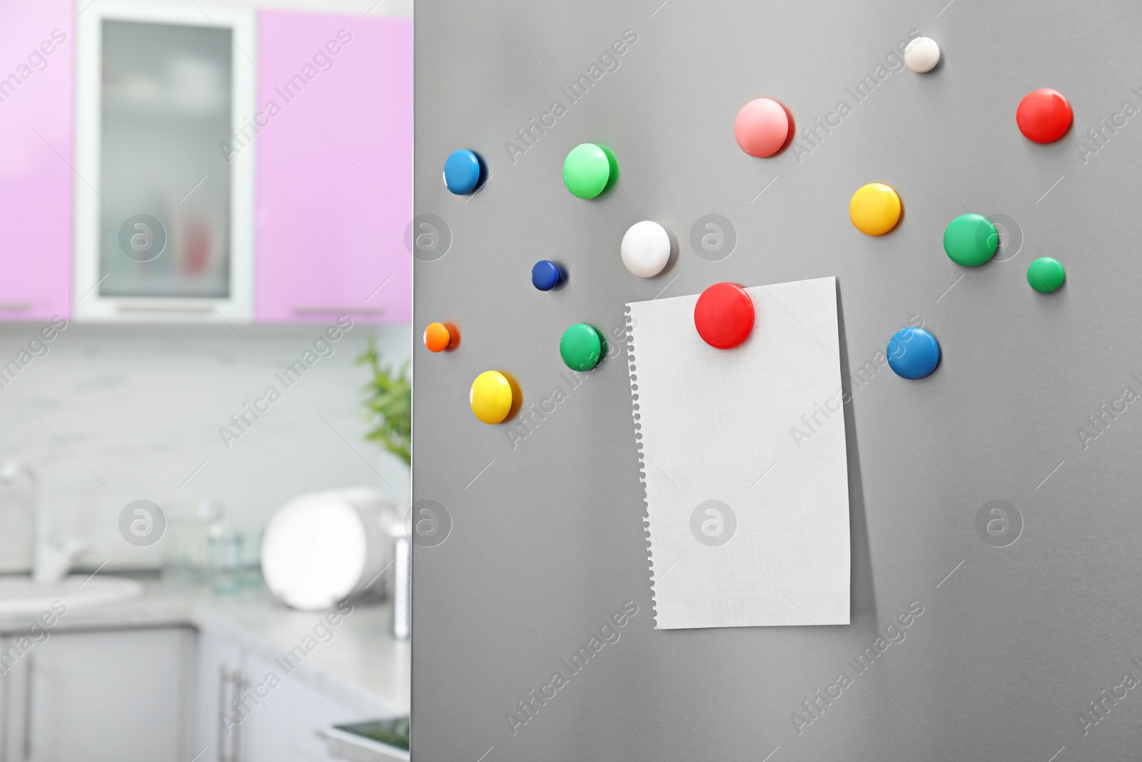 Photo of Empty sheet of paper with colorful magnets on refrigerator door in kitchen. Space for text