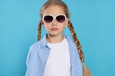 Girl in stylish sunglasses on light blue background