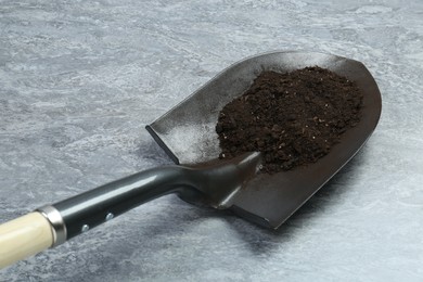 Photo of Metal shovel with fertile soil on gray textured surface