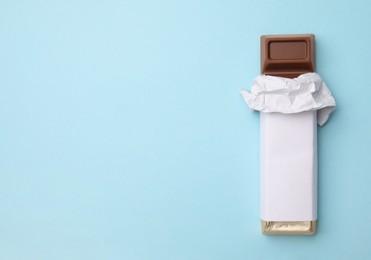 Photo of Tasty chocolate bar in package on light blue background, top view. Space for text