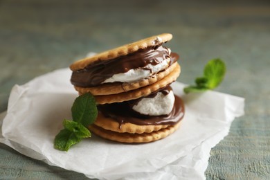 Photo of Delicious marshmallow sandwiches with crackers, mint and chocolate on light blue wooden table, closeup