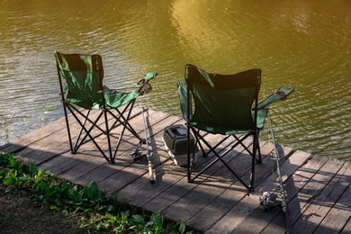 Folding chairs, tackle box and rods for fishing on wooden pier at riverside. Recreational activity