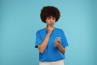 Photo of Thoughtful young woman with smartphone on light blue background