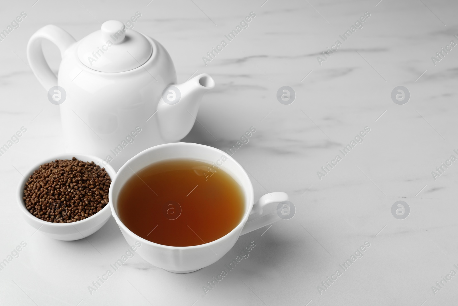 Photo of Delicious buckwheat tea and granules on white marble table. Space for text