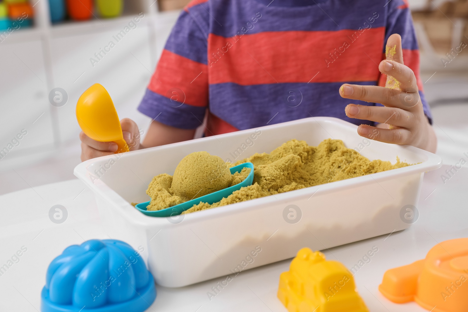 Photo of Little boy playing with bright kinetic sand at table in room, closeup