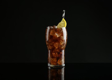 Glass of refreshing soda water with ice cubes and lemon slice on black background