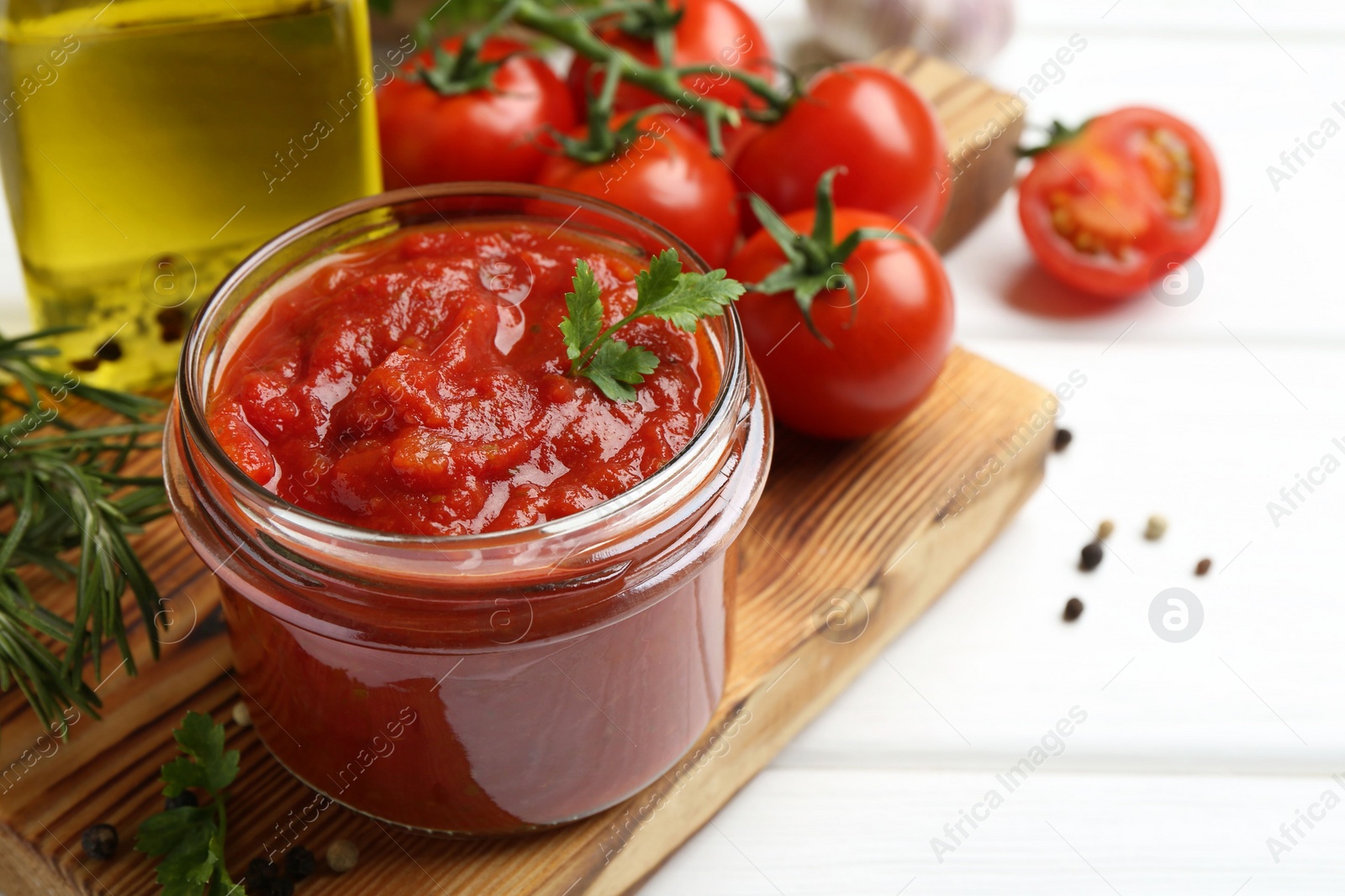 Photo of Homemade tomato sauce in jar and fresh ingredients on white wooden table, closeup