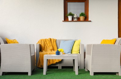 Beautiful rattan garden furniture, soft pillows, blanket and yellow chrysanthemum flowers outdoors