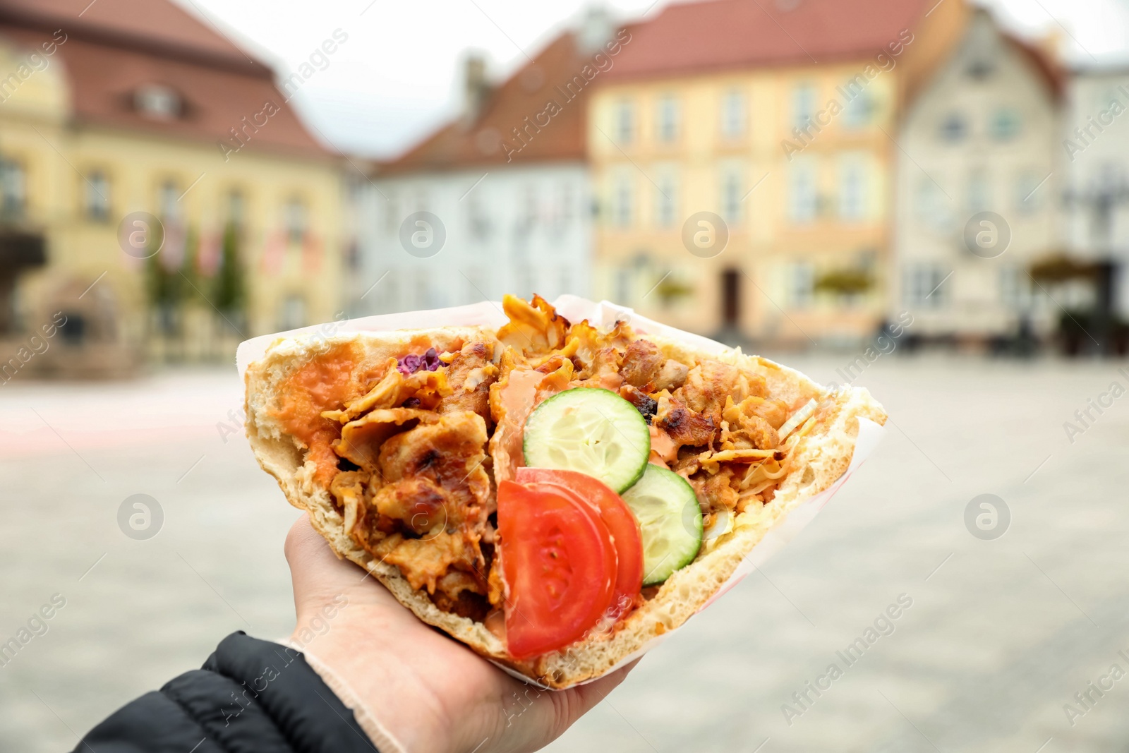 Photo of Woman holding delicious bread with roasted meat and vegetables outdoors, closeup. Street food