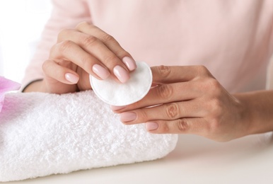 Photo of Woman removing polish from nails with cotton pad at table, closeup