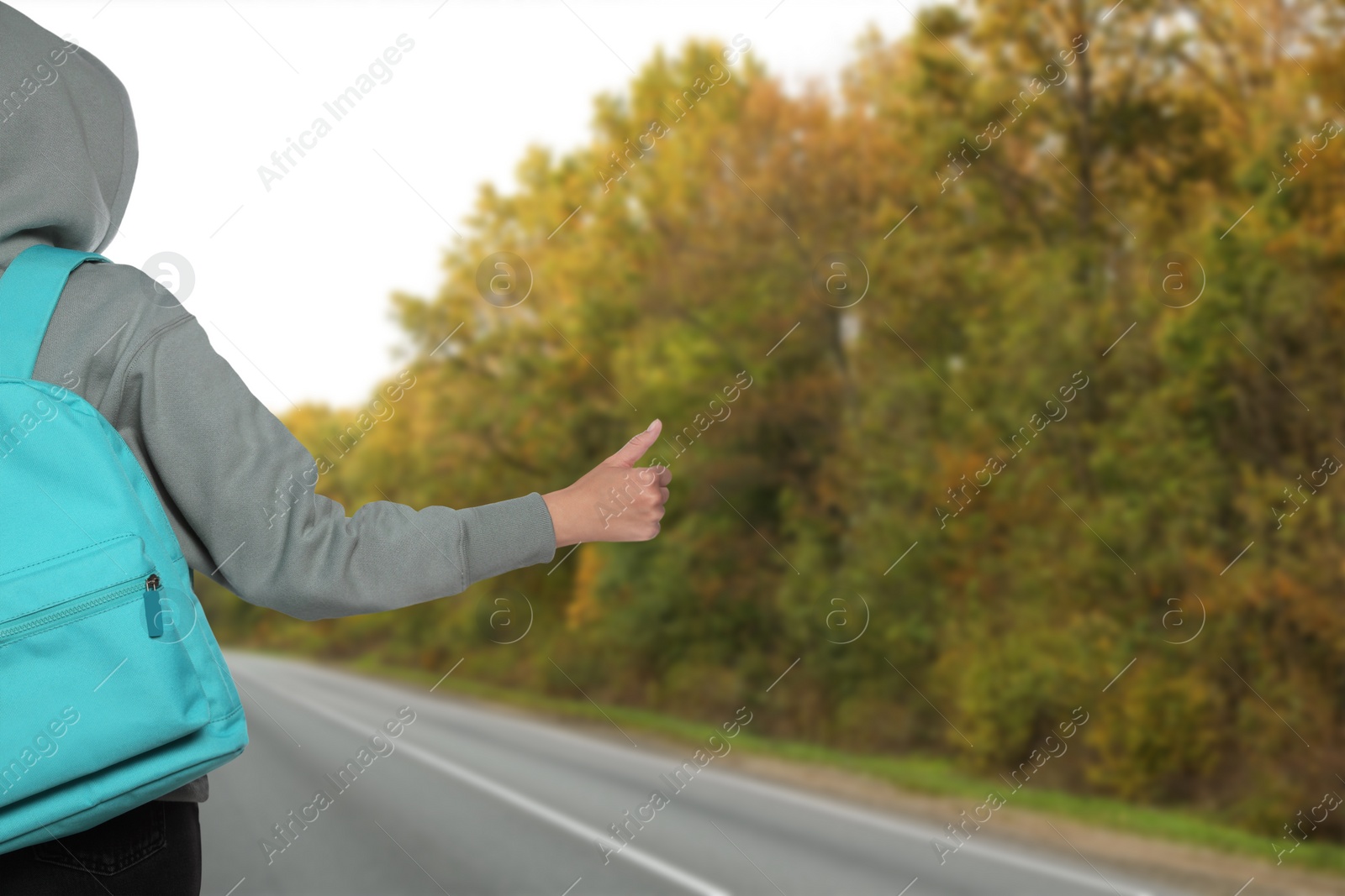 Image of Woman with backpack catching car on road, closeup. Hitchhiking trip