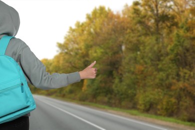 Woman with backpack catching car on road, closeup. Hitchhiking trip