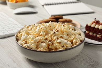 Photo of Bad eating habits at workplace. Delicious popcorn in bowl on white wooden table, closeup