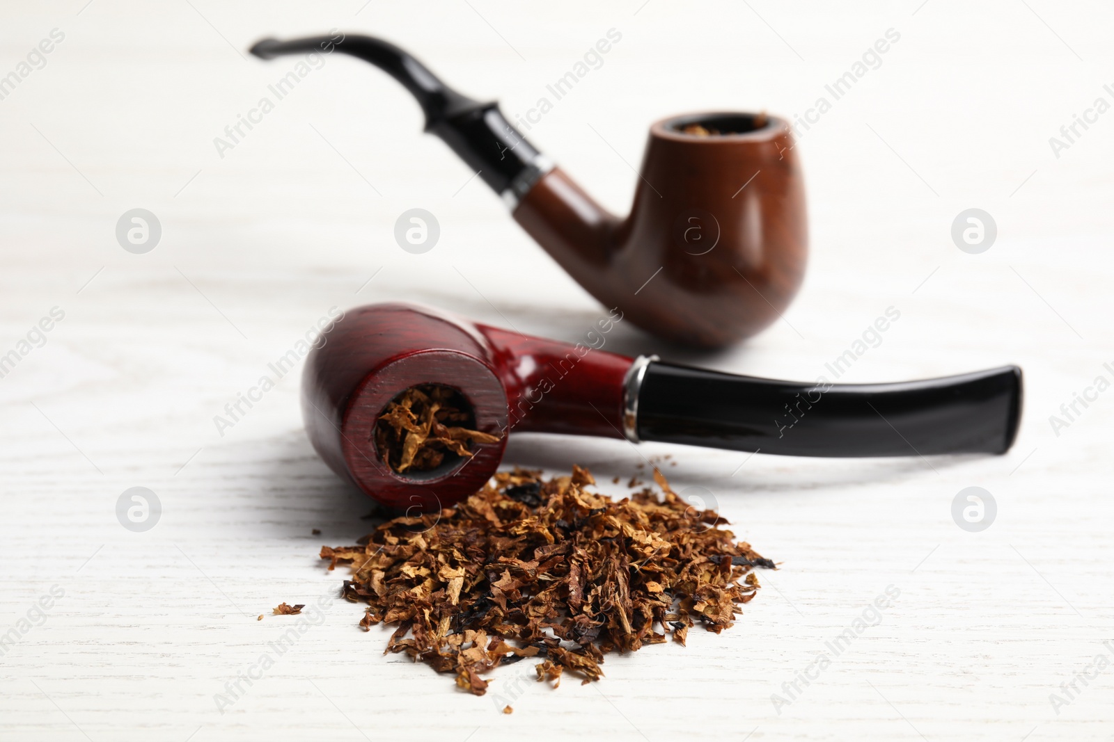 Photo of Smoking pipes with tobacco on white wooden table