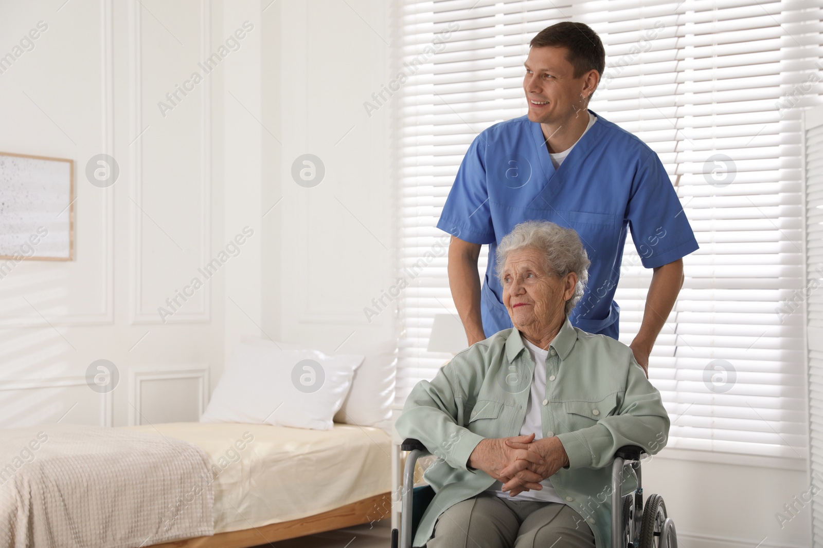 Photo of Caregiver assisting senior woman in wheelchair indoors. Home health care service