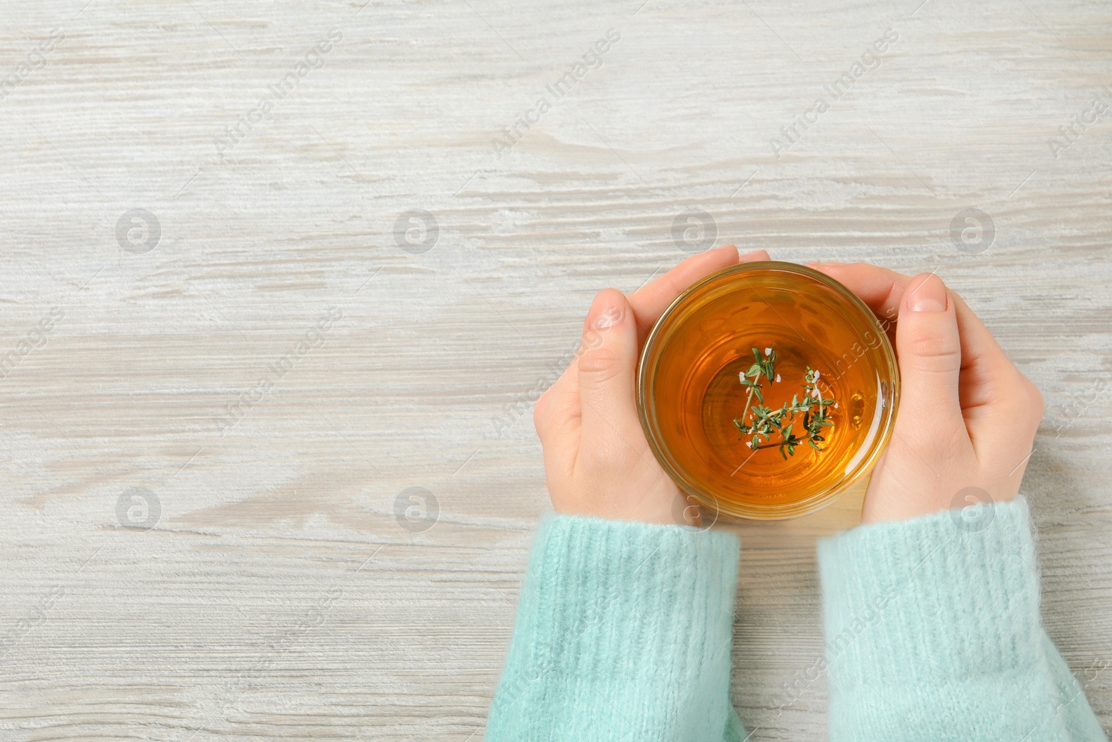 Photo of Woman holding cup of tasty herbal tea with thyme at white wooden table, closeup. Space for text